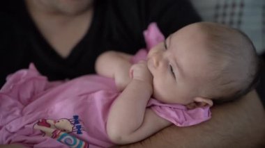 Yeni doğmuş bebek babasının kollarında yatıyor ve yumruklarını çiğniyor.