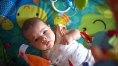 Yeni doğmuş bebek bir oyun hasırının üzerinde uzanıyor ve kolları ve bacaklarıyla sallanıyor.