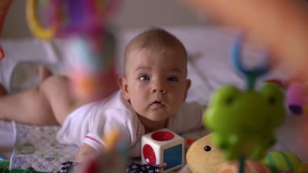 Baby ligt op het bed en raakt de kubus met haar handen — Stockvideo