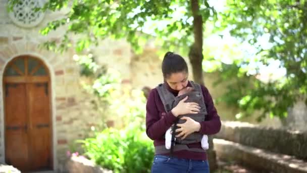 Moeder knuffelt en kust een pasgeboren baby in een draagdoek in het park — Stockvideo