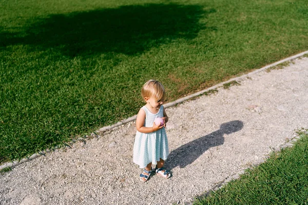 彼女の手にボールを持つ女の子は芝生の砂利道に立っています — ストック写真