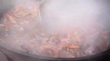 Dumanı tüten Özbek pilavını kazanda dekolteli kaşıkla karıştırmak