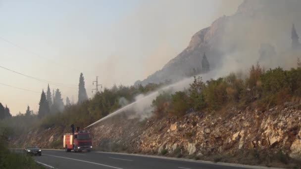 Bombeiros em um caminhão de bombeiros extinguem um incêndio florestal no sopé das montanhas montenegrinas — Vídeo de Stock
