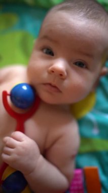 Yeni doğan elinde çıngırakla yatakta yatıyor. Yakın plan.