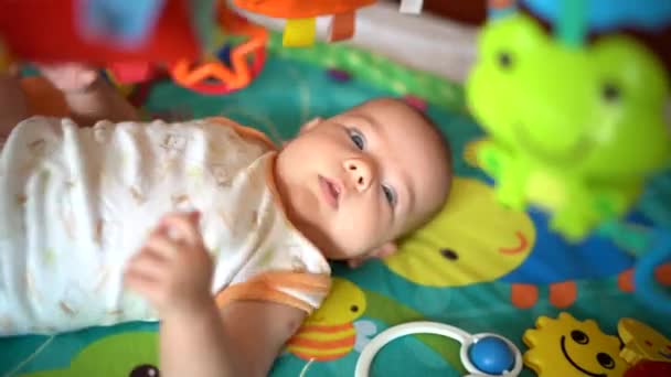 Neugeborenes ruckelt mit Händen und Füßen auf der Spielmatte und betrachtet hängendes Spielzeug — Stockvideo