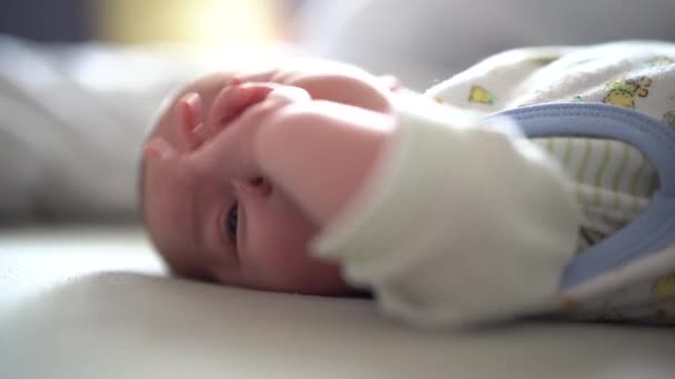 Baby ligt op het bed en raakt zijn gezicht met zijn hand — Stockvideo