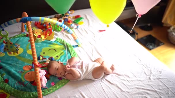 Pasgeborene ligt op een speelkameraadje met ballonnen vastgebonden aan zijn armen en benen — Stockvideo