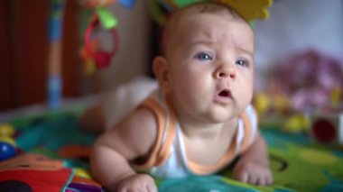 Yenidoğan midesi oyun hasırının üzerinde yatar ve etrafına bakar.