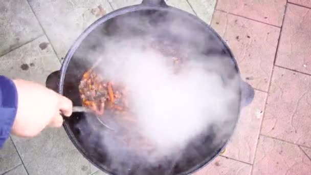 Keverés üzbég pilaf egy hasított kanállal egy nagy üstben — Stock videók
