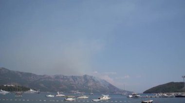 Budva 'nın yukarısındaki dağlardan çıkan dumanlar denizdeki yatların zeminine vuruyor.