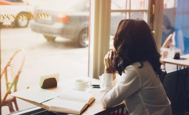 Woman sits in a cafe with a cup of coffee, tea. Read a book and dream. Look  out the window. Wait for somebody.