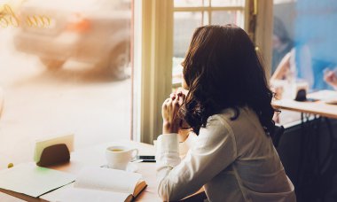 Woman sits in a cafe with a cup of coffee, tea. Read a book and dream. Look  out the window. Wait for somebody.