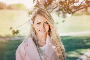 Çiçek Bahçe ile poz pembe bir ceket genç güzel kadın. Park.