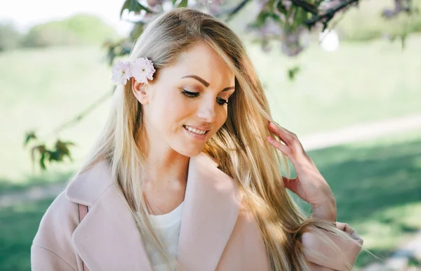 Donna con lunghi capelli biondi in giardino con fiori. Bella ragazza in una giornata di sole . — Foto Stock