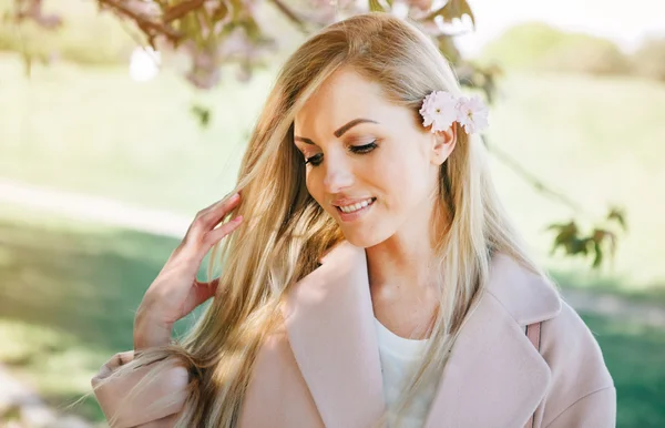 Mulher com longos cabelos loiros no jardim com flores. Menina bonita em um dia ensolarado . — Fotografia de Stock