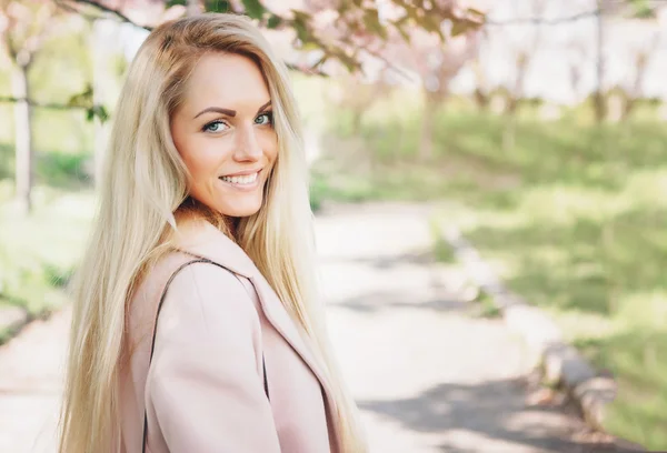 Giovane bella donna in un cappotto rosa in posa con fiori in giardino. Parco . — Foto Stock