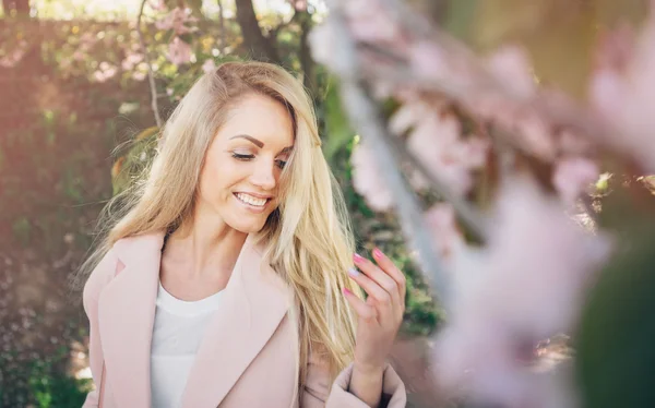 Mooie jongedame in een roze jas poseren met bloemen in de tuin. Park. — Stockfoto