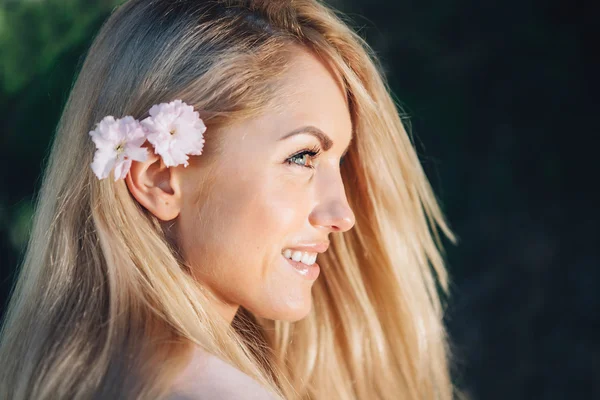 Kobieta z długimi blond włosami w ogrodzie z kwiatami. Piękna dziewczyna w słoneczny dzień. — Zdjęcie stockowe
