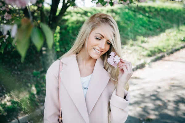 Mooie jongedame in een roze jas poseren met bloemen in de tuin. Park. — Stockfoto