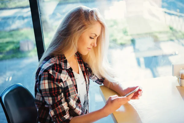 Junge Studentin sitzt in modernem Café mit Handy. Sonnenuntergang. Frau sitzt vor dem Fenster im Café. — Stockfoto