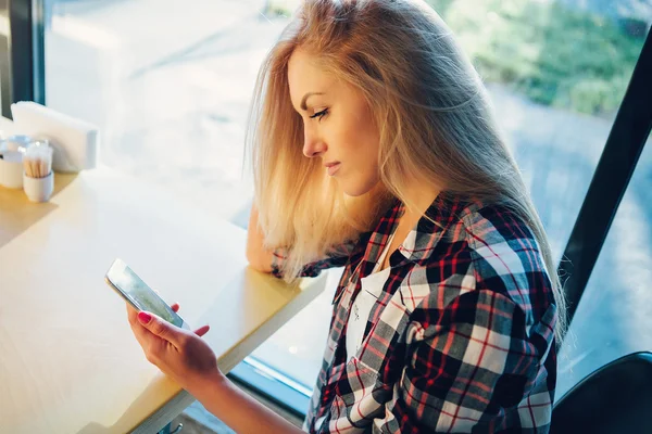 Junge Studentin sitzt in modernem Café mit Handy. Sonnenuntergang. Frau sitzt vor dem Fenster im Café. — Stockfoto