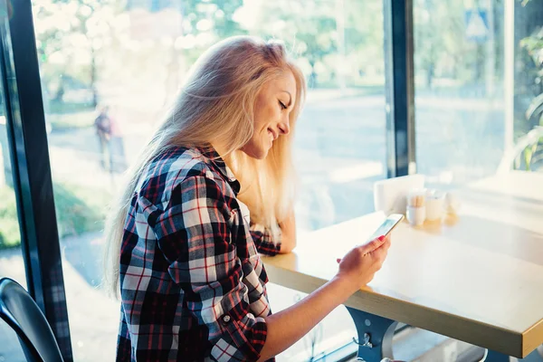 Junge Studentin sitzt in modernem Café mit Handy. Sonnenuntergang. Frau sitzt vor dem Fenster im Café. — Stockfoto