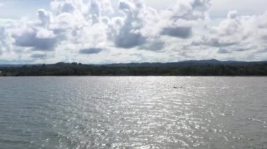 Karayip sahillerinde dron, arkasında dağlar ve suda yelkenli.