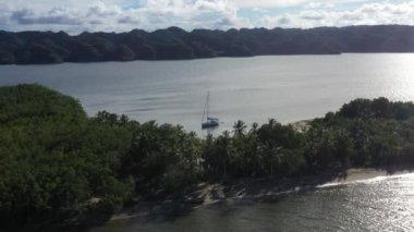 Karayip sahillerinde droni, dağların arkasında ve suda yelkenli.