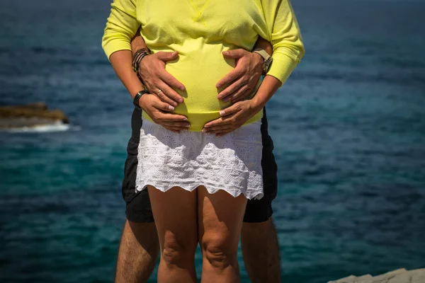 Mulher grávida e seu marido segurando as mãos em seu bebê bum — Fotografia de Stock
