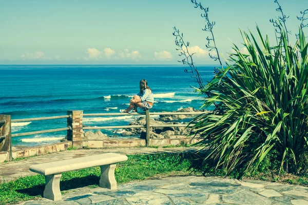 Young woman sitting on bench facing the sea — Stock Photo, Image