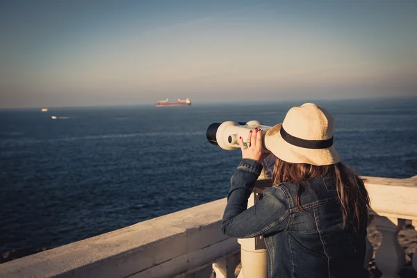 Young girl looking through a coin operated binoculars on the sea — Stock Photo, Image