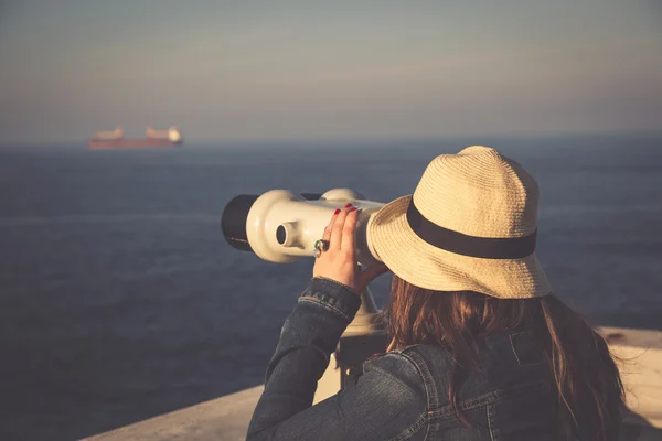 Young girl looking through a coin operated binoculars on the sea — Stock Photo, Image