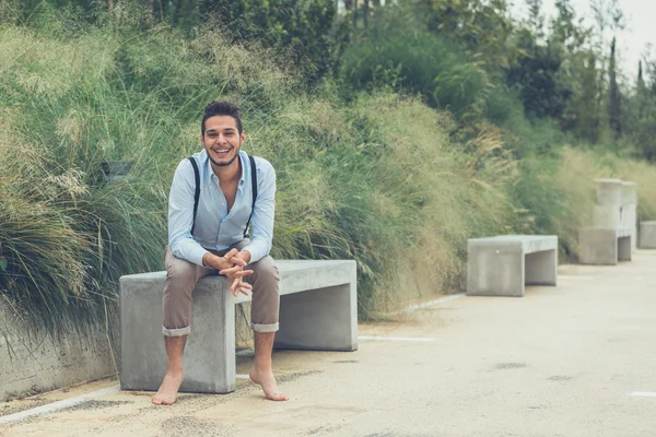 Jovem homem bonito sentado em um banco de concreto — Fotografia de Stock