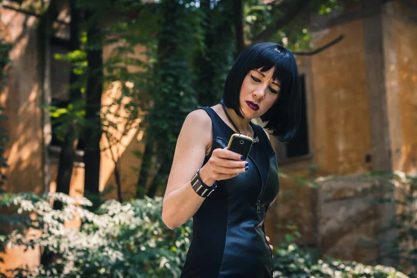 Pretty goth girl using phone in a city park — Stock Photo, Image