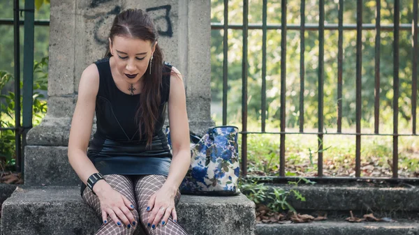 Mooie goth meisje zit in een stadspark — Stockfoto