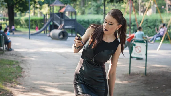 Mooi goth meisje met behulp van telefoon in een stadspark — Stockfoto