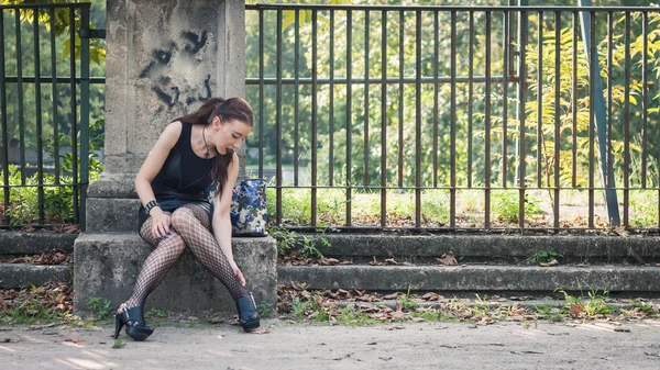 Pretty goth girl sitting in a city park — Stock Photo, Image