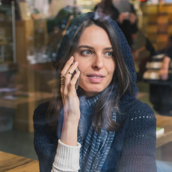 Beautiful girl talking on phone behind a window — Stock Photo, Image