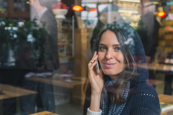 Menina bonita falando no telefone atrás de uma janela — Fotografia de Stock