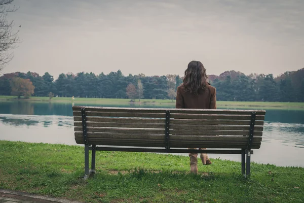 Vacker ung kvinna sitter på en bänk i en park — Stockfoto