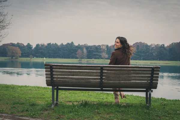 Mulher bonita sentada em um banco em um parque da cidade — Fotografia de Stock