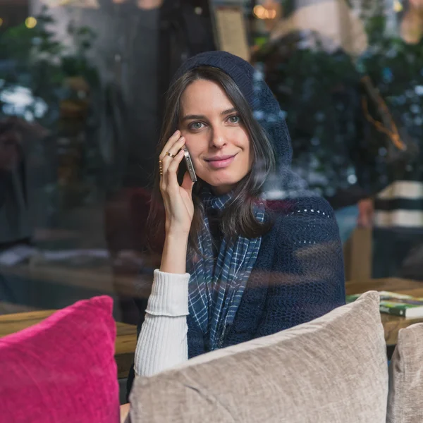 Menina bonita falando no telefone atrás de uma janela — Fotografia de Stock