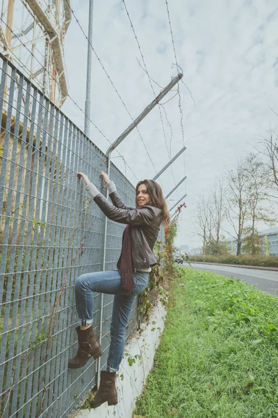 Beautiful young brunette climbing over a fence — Stock Photo, Image