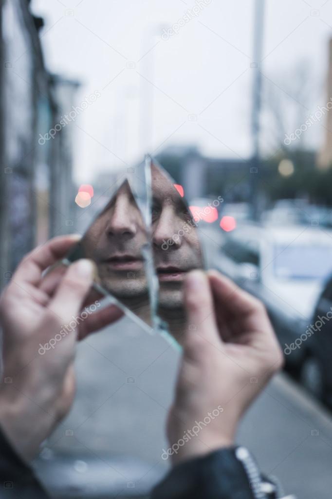 Punk guy looking at himself in a shattered mirror