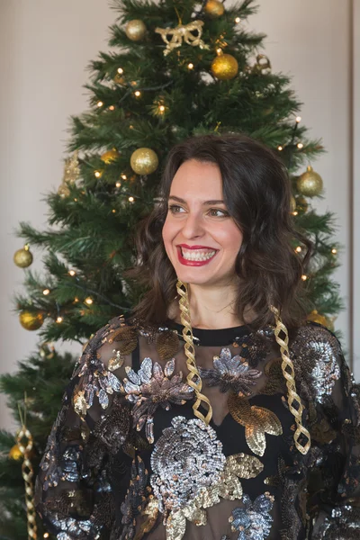 Beautiful young brunette posing in front of a Christmas tree — Stock Photo, Image