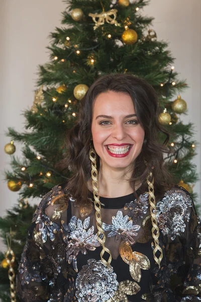 Vacker ung brunett poserar framför en julgran — Stockfoto