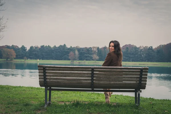 Wanita muda cantik duduk di bangku di taman kota — Stok Foto