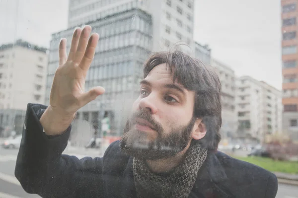 Young handsome bearded man posing behind a glass — Stock Photo, Image