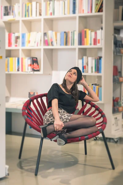 Beautiful young brunette sitting in a bookstore — Stock Photo, Image