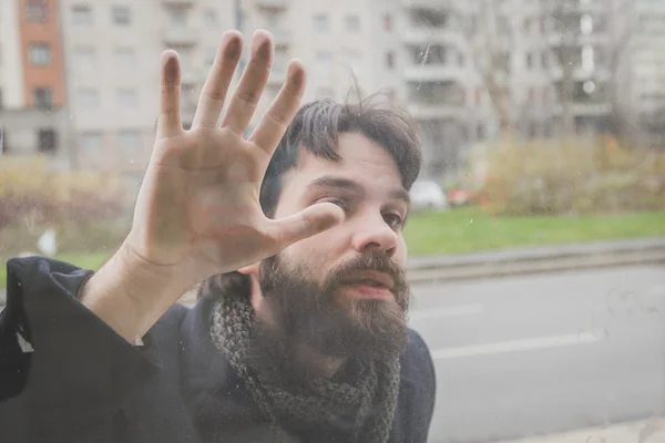Genç yakışıklı sakallı adam bir camın arkasında poz — Stok fotoğraf